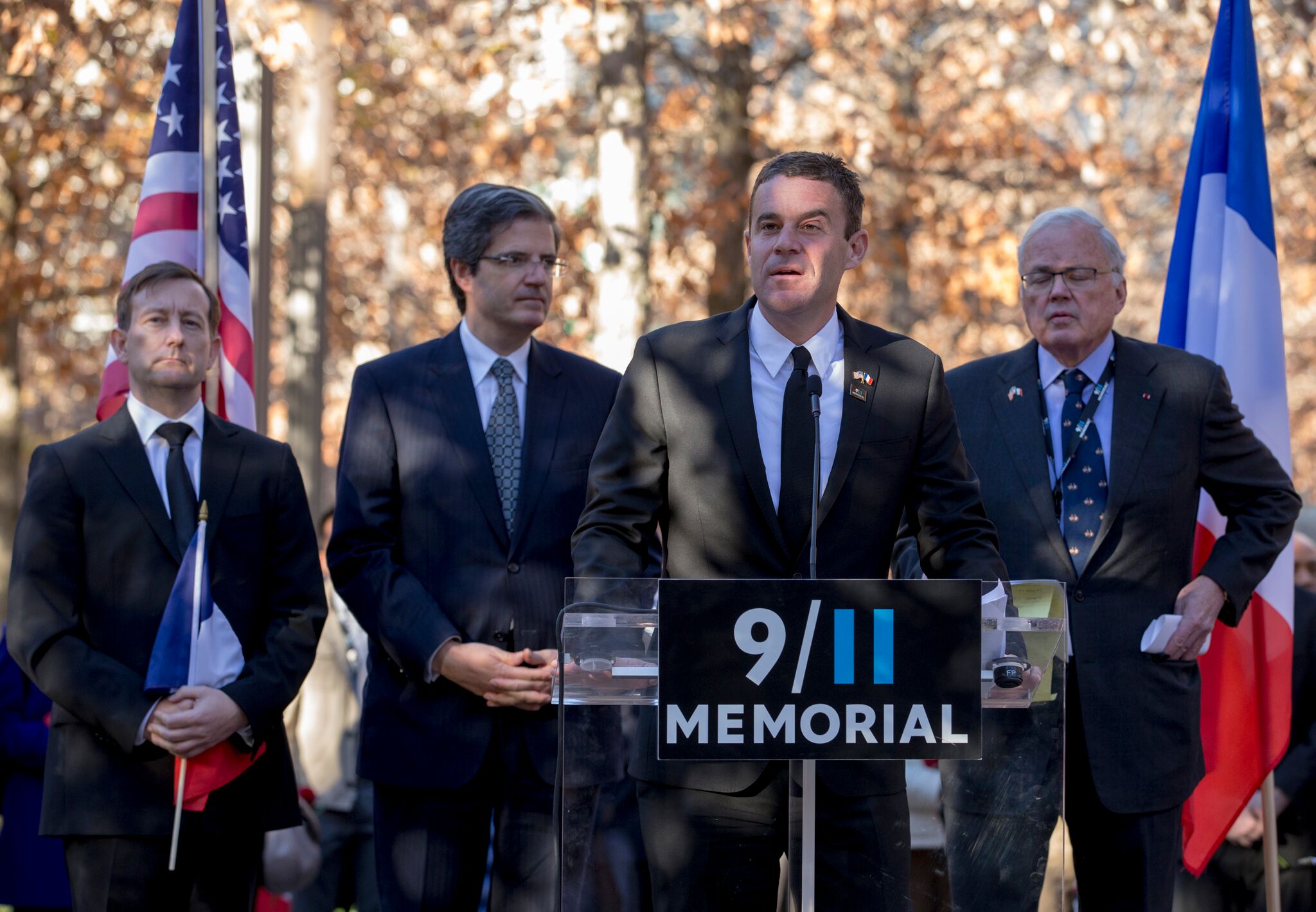 Joe Daniels speaking at a remembrance gathering at the 9/11 Memorial, with French and U.S. flags